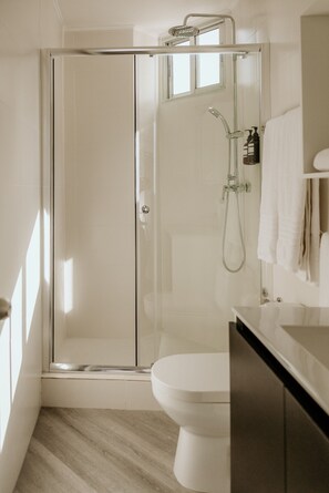 Een moderne badkamer met een glazen douchecabine, een wit toilet en een houten vloer.