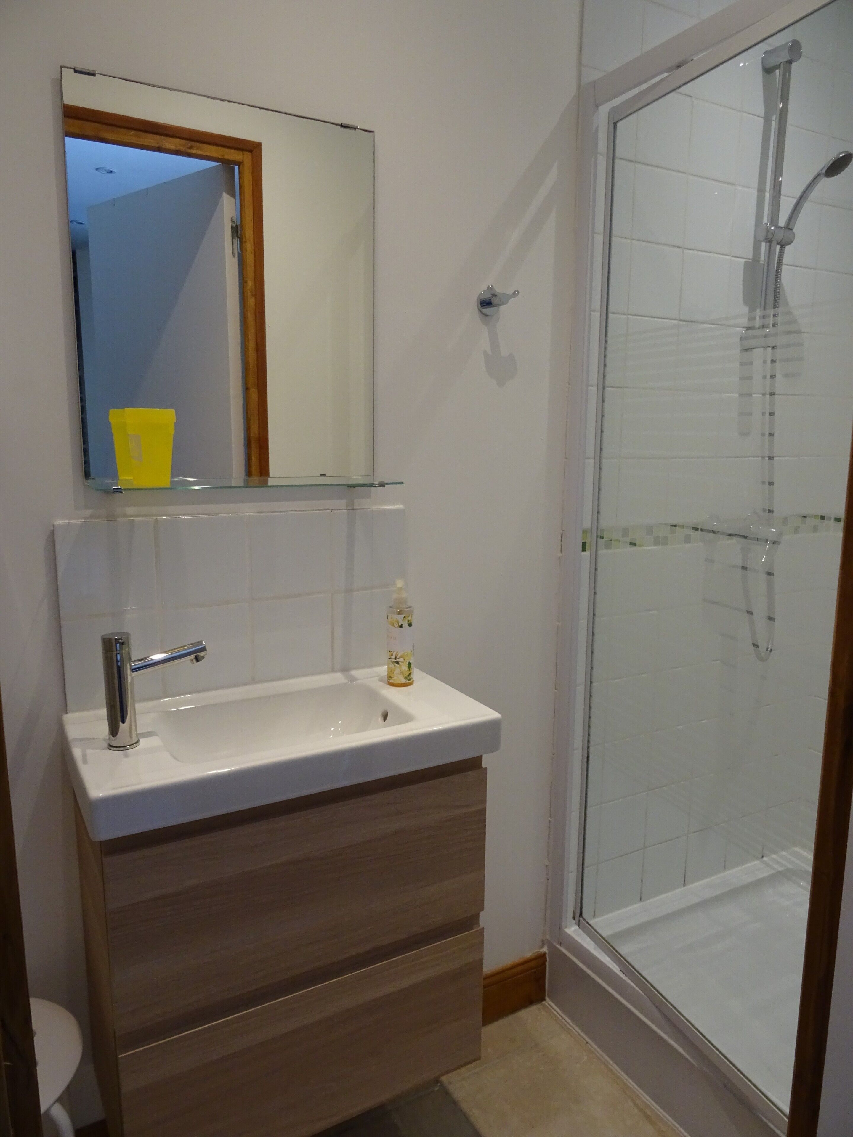 Une salle de bain avec un lavabo blanc, un miroir, une tasse jaune et une cabine de douche en verre.