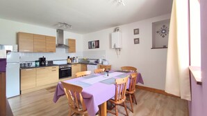 A compact kitchen with wooden cabinets, a dining table with chairs, and a built-in oven. - Gîte Lavande - Pen Ar Voas Gîtes with Private Terrace, Shared Garden, and Wi-Fi (Plestin-les-Grèves)