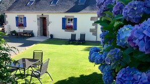 A house with a sloped roof, stone walls, a front porch with a bench, and a well-maintained lawn. - Gîte Lavande - Pen Ar Voas Gîtes with Private Terrace, Shared Garden, and Wi-Fi (Plestin-les-Grèves)