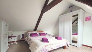 A bedroom with a sloped ceiling, a bed with purple bedding, a white wardrobe, and a mirror cabinet. - Gîte Lavande - Pen Ar Voas Gîtes with Private Terrace, Shared Garden, and Wi-Fi (Plestin-les-Grèves)