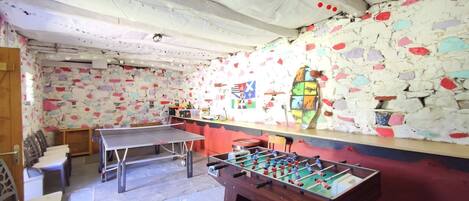 A room with a foosball table, ping pong table, and a stone wall with colorful decorations.