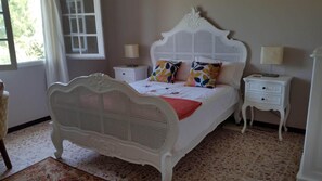 Una camera da letto con un letto bianco, due comodini, una finestra e una sedia.