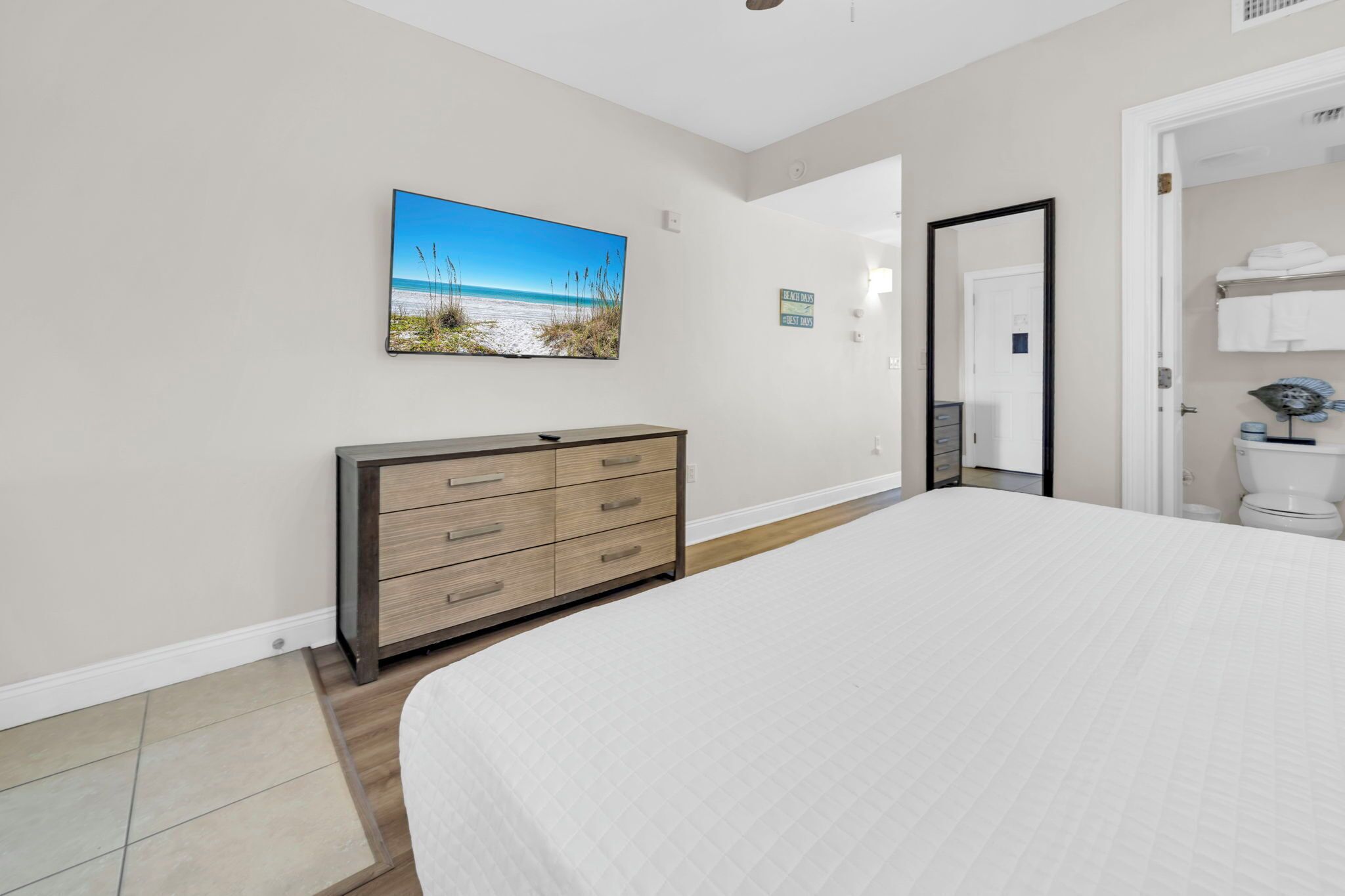 A bedroom with a bed, a dresser, a painting, and a bathroom visible through an open door.