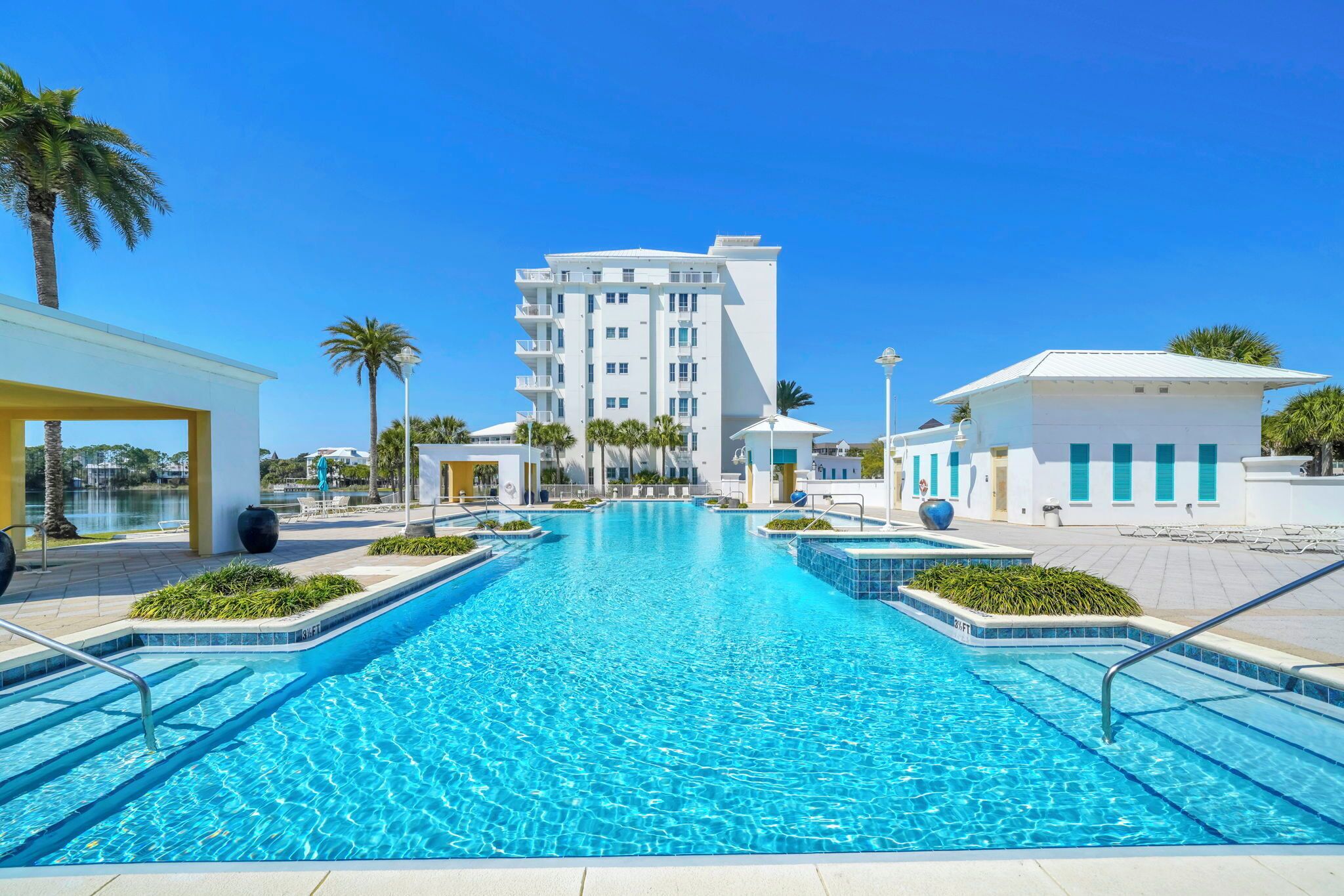 A swimming pool with clear blue water, surrounded by a modern building with balconies and a clear sky.