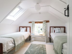 A bedroom with two beds, a window with curtains, a desk with a lamp, and a ceiling light. - Pigwig Cottage (Matlock)