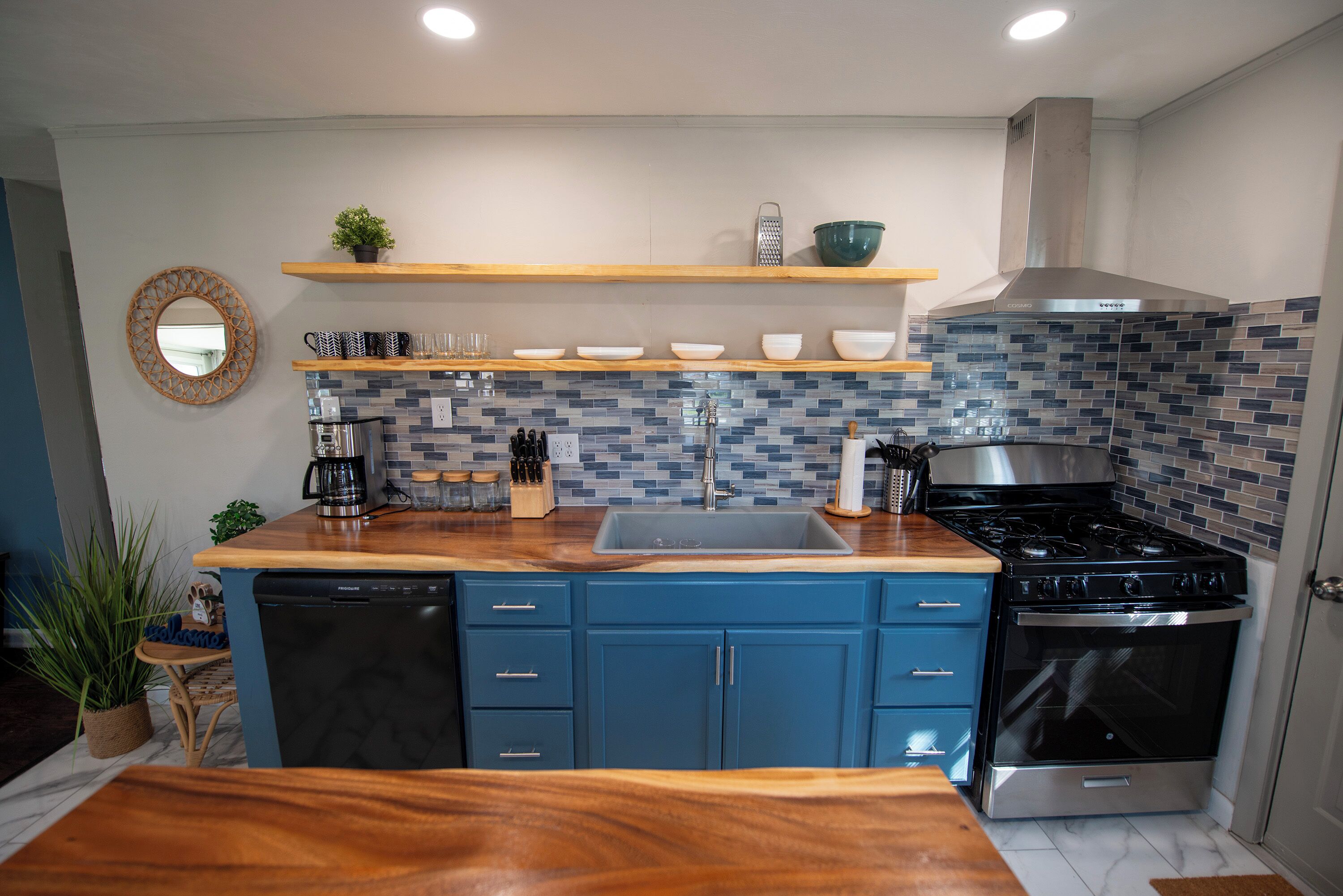 A modern kitchen with blue cabinets, a stainless steel stove, and a tiled backsplash.