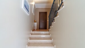 Eine Treppe führt zu einer Tür mit Holzoptik, weißen Wänden und einem hellen Boden.