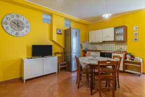 A kitchen with yellow walls, a stainless steel refrigerator, a dining table with chairs, a television on a cabinet, and a clock on the wall. - Apartment 'Plutone with Sea View Terrace', Wi-Fi and Air Conditioning (Portopalo di Capo Passero)