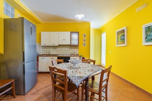A kitchen with a refrigerator, cabinets, and a dining table with chairs. - Apartment 'Plutone with Sea View Terrace', Wi-Fi and Air Conditioning (Portopalo di Capo Passero)