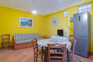 A dining area with a table, chairs, a sofa, a clock, and a refrigerator. - Apartment 'Plutone with Sea View Terrace', Wi-Fi and Air Conditioning (Portopalo di Capo Passero)
