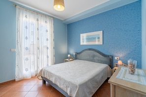 A bedroom with a bed, a nightstand, a lamp, a framed picture on the wall, and a window with curtains. - Apartment 'Plutone with Sea View Terrace', Wi-Fi and Air Conditioning (Portopalo di Capo Passero)