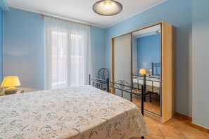 A bedroom with a bed, a bedside table, a lamp, a window with curtains, and a mirror. - ‘Saturno’ Apartment Steps from the Sea with Balcony, Wi-Fi & Air Conditioning (Portopalo di Capo Passero)