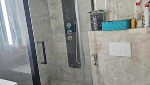 A bathroom with a glass-enclosed shower, a white toilet, and a marble-tiled wall. - Chambre Lit double (Dunkirk)