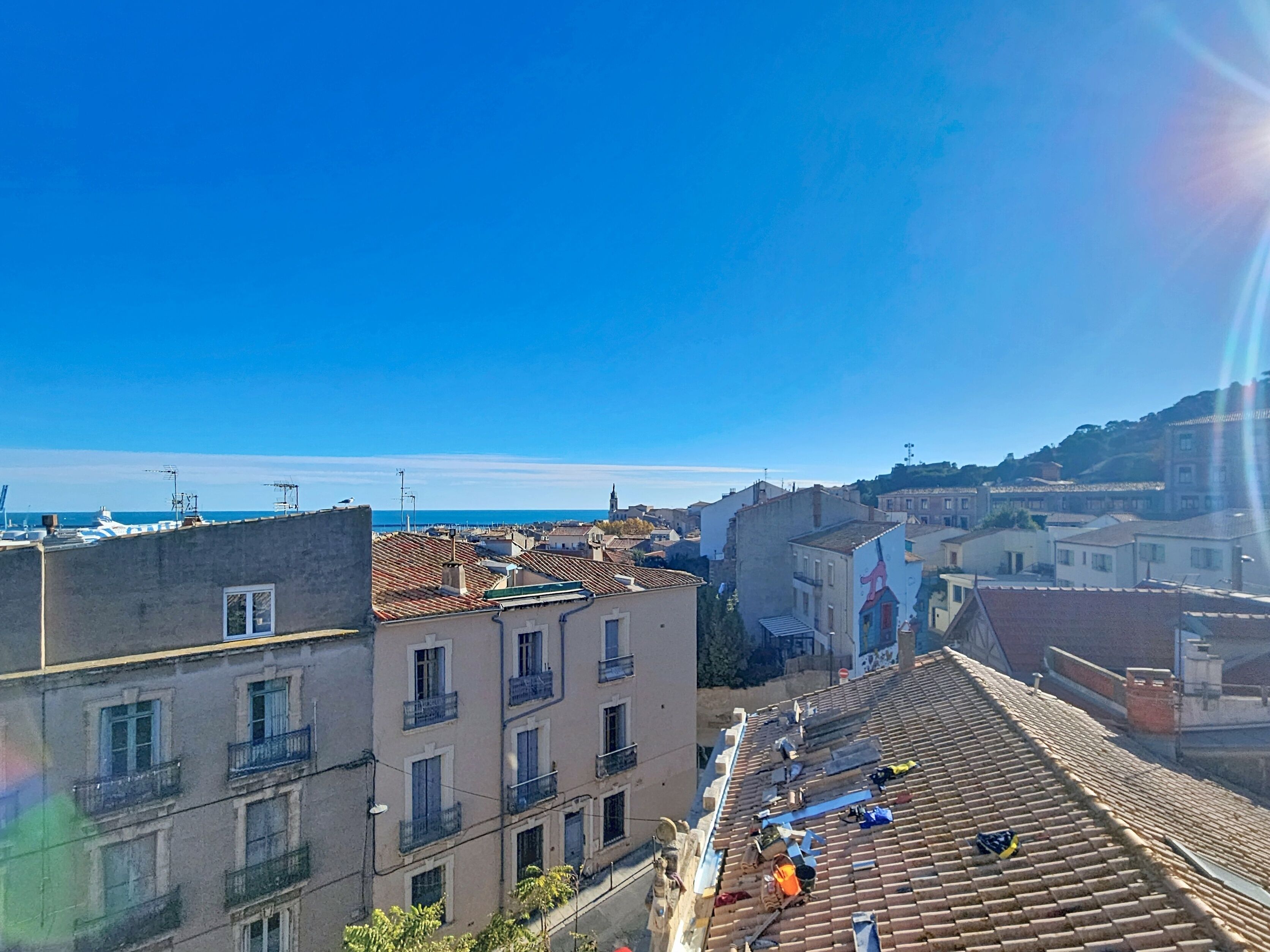 A coastal cityscape with buildings, a clear sky, and a distant view of the sea.