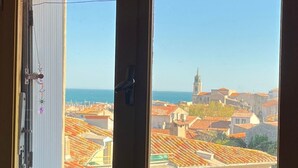 A window with a view of a coastal town, a building with a tower, and a clear sky. - 5-minute walk from the town center, magnificent view of the sea and the old town (Sète)
