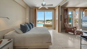 Un dormitorio con cama, escritorio, silla, ventilador de techo y vistas a una piscina y playa.