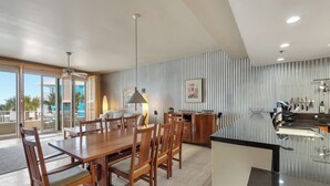 Una cocina moderna con una isla grande, una mesa de comedor de madera y sillas, con vista a la piscina exterior.