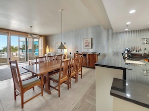 A modern kitchen with a large island, wooden dining table, and chairs, with a view of the pool outside. - Joes Place- Belle Mer 3/3 Condo with ground floor access! (Navarre Beach)