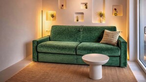 Een groene bank met een witte bijzettafel, een wandplank met vazen, en een raam met uitzicht.