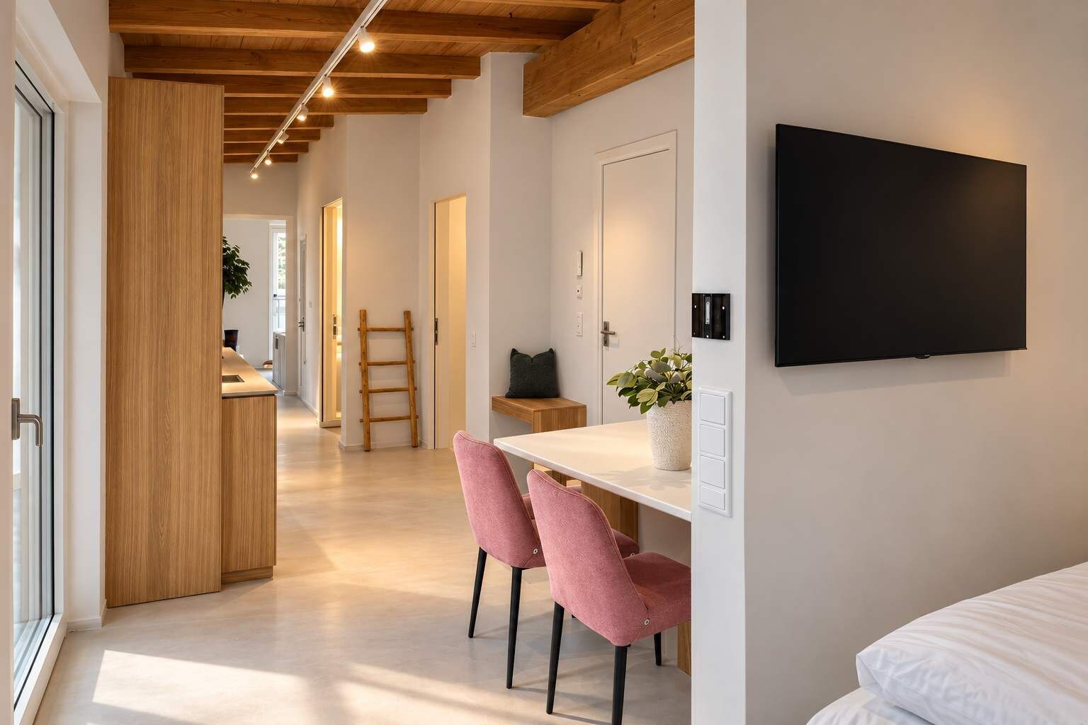 En modern inredning med ett träpanelat tak, en platt-TV som är monterad på väggen, en matplats med rosa stolar och en köksbänk.