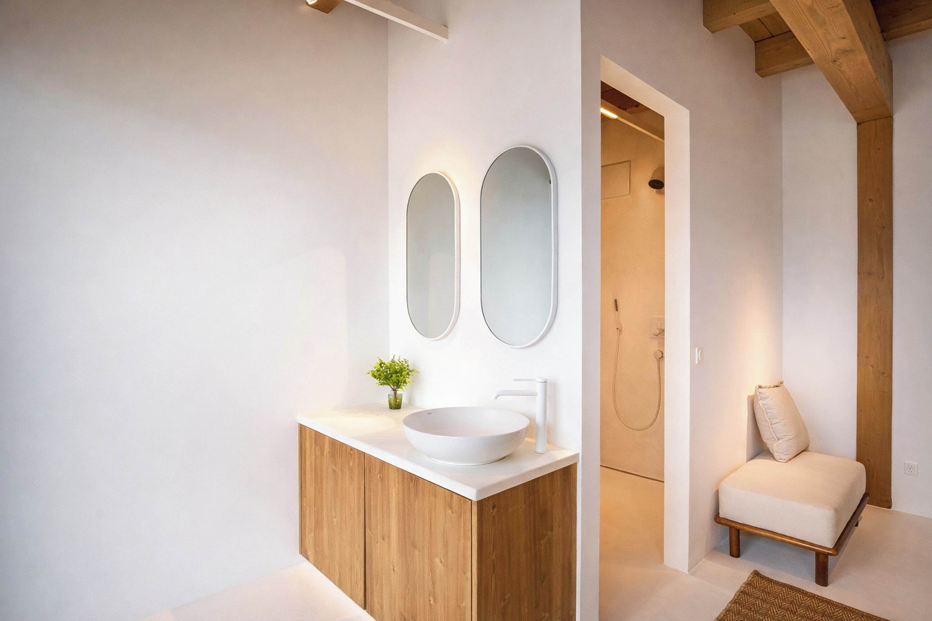 Une salle de bain moderne avec un meuble-lavabo en bois, un lavabo blanc, deux miroirs et une petite plante.