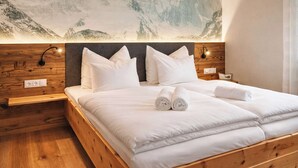 A double bed with white linens and two rolled towels, a wooden headboard, a wall-mounted light, and a mountain landscape mural. - ZWEITE HEIMAT – Cozy Apartment with Garden (Fügen)
