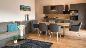 A modern kitchen with dark cabinets, a wooden dining table, and a hanging light fixture. - ZILLERHEART – Apartment with Balcony & Mountain View (Fügen)