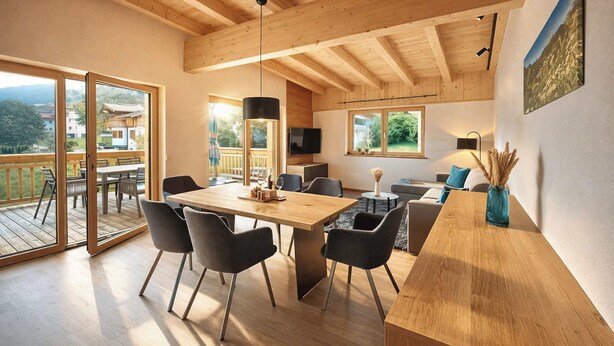 A spacious room with a wooden ceiling, a large dining table, and a view of the outdoors. - ZILLERHEART – Apartment with Balcony & Mountain View (Fügen)