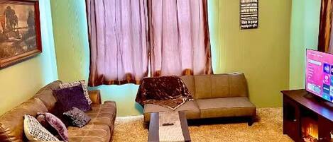 Uma sala de estar com sofá, mesa de centro, televisão e lareira.