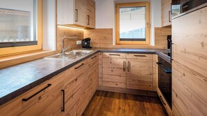 A modern kitchen with wooden cabinetry, a stainless steel sink, and a Bosch coffee maker. - BEIM LOIS Dorfblick – 2 Floors & Sauna Access (Gerlos)