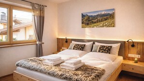 Un letto con lenzuola bianche, una coperta in pelliccia e un dipinto che raffigura un paesaggio montano.