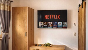 Una stanza con un armadio in legno, una cassettiera in legno e una TV a parete con Netflix che mostra diverse serie.