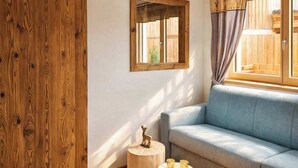 Una stanza con parete in legno, una finestra che si affaccia su una recinzione di legno, un divano blu e due sgabelli di legno con una statuetta di cervo e candele.