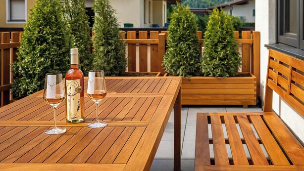 Un tavolo di legno con due bicchieri da vino e una bottiglia su un balcone con mobili in legno e piante in vaso.