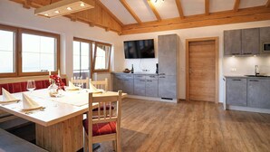 A spacious kitchen with wooden beams, a dining area with a table set for four, and a large window providing natural light. - HOCHEBEN – Balcony & Private Sauna (Ramsau im Zillertal)