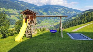 A playground with a slide, swing, and trampoline, set against a mountainous backdrop. - HOCHEBEN – Balcony & Private Sauna (Ramsau im Zillertal)