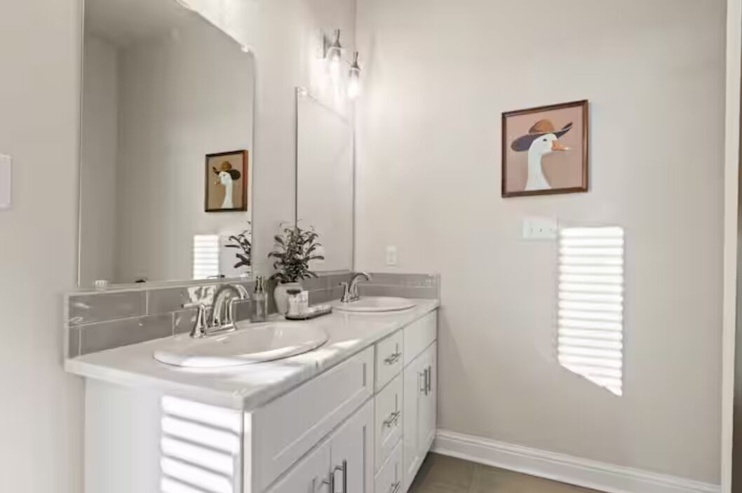 A bathroom with a double sink vanity, a large mirror, and a framed picture on the wall.