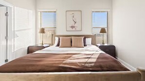 A bedroom with a large bed, two bedside tables, a wall-mounted artwork, and a window with blinds. - Crawfish House (Youngsville)