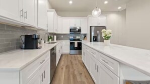 A modern kitchen with white cabinets, stainless steel appliances, and a wooden floor. - Crawfish House (Youngsville)