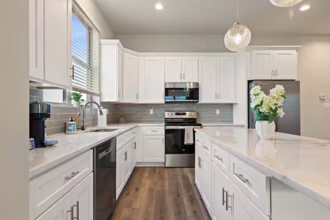 A modern kitchen with white cabinetry, stainless steel appliances, and a wooden floor.