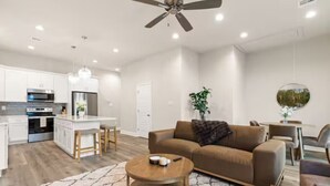 A modern kitchen with white cabinets, a central island, and a dining area with a round table and chairs. - Crawfish House (Youngsville)