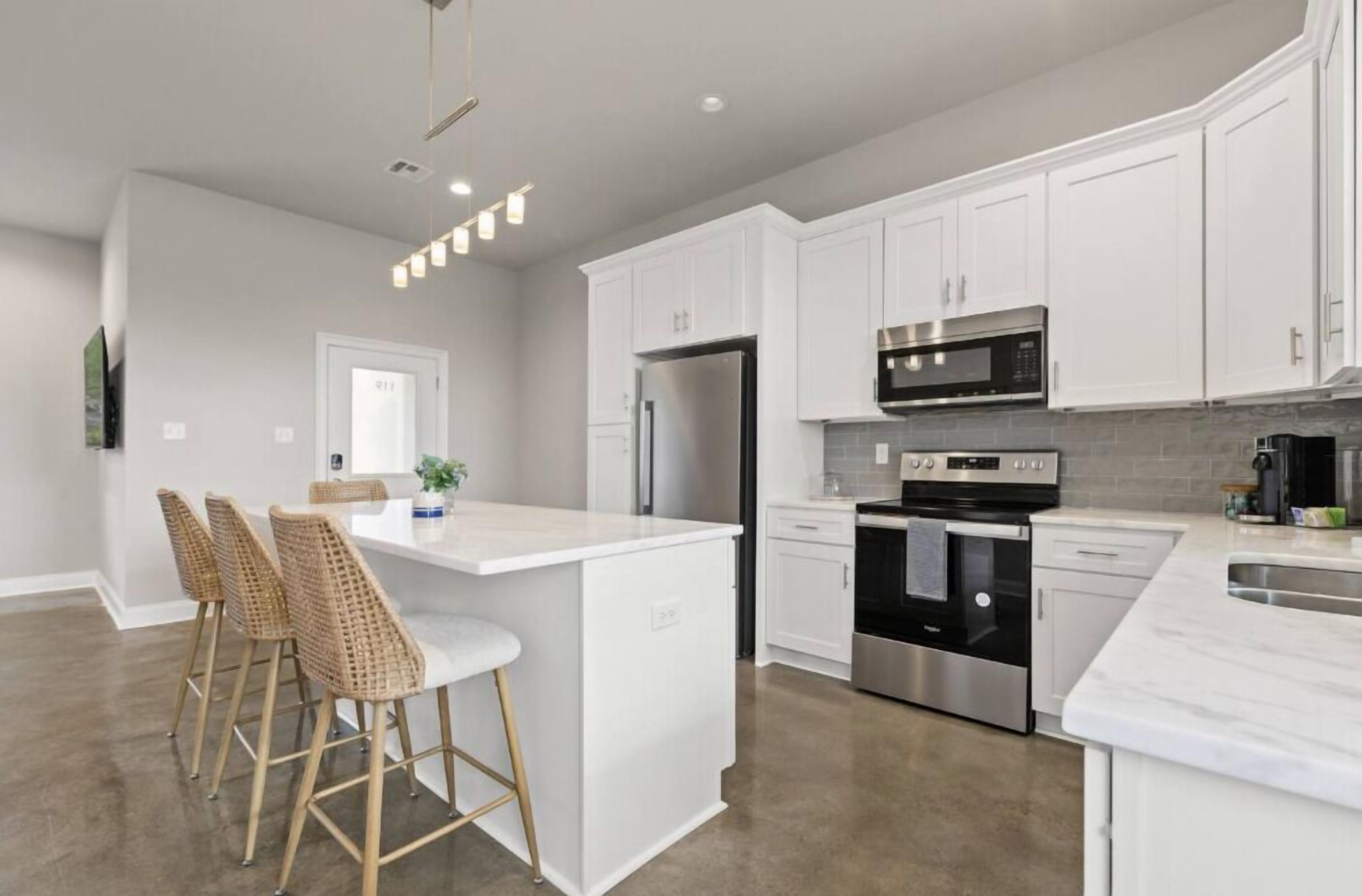 A modern kitchen with white cabinets, stainless steel appliances, and a central island with bar stools.