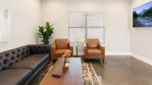 A living room with a black leather sofa, two brown leather armchairs, a wooden coffee table with a vase, a small table with a glass top, and a painting on the wall. - Crawfish House (Youngsville)
