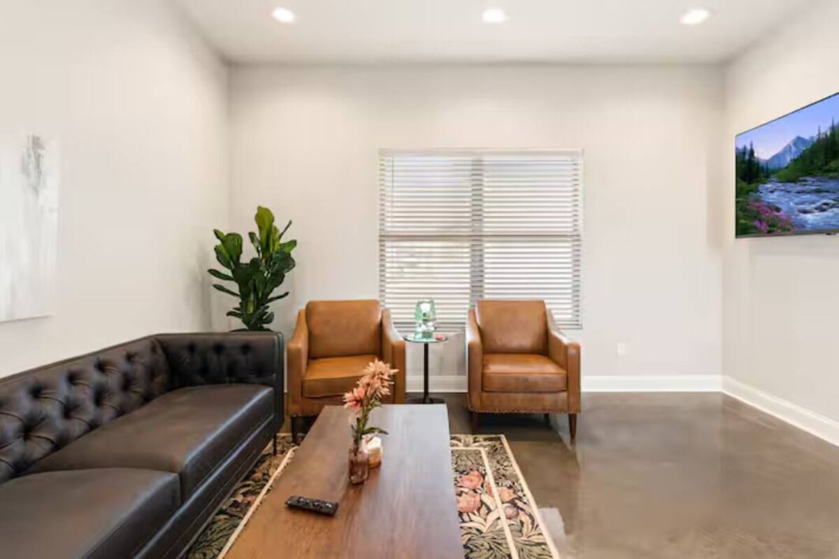 A living room with a black leather sofa, two brown leather armchairs, a wooden coffee table with a vase, a small table with a glass top, and a painting on the wall.