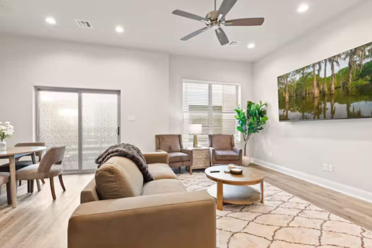 A living room with a sofa, chairs, a coffee table, a ceiling fan, and a painting on the wall.