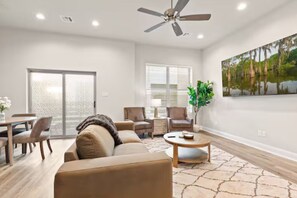 Un salon comprenant un canapé, des fauteuils, une table basse, un ventilateur de plafond et un tableau accroché au mur.