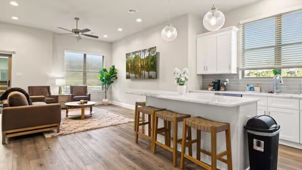 A modern kitchen with white cabinets, a bar area, and a dining space with a sofa and chairs. - Crawfish House (Youngsville)
