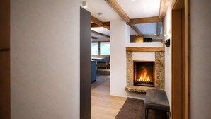 A modern interior with a stone fireplace, wooden beams, and a view to a dining area. - RACING Suite – Terrace & Sauna Access (Kleinboden)