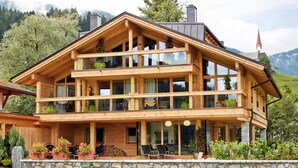 A multi-story wooden chalet with balconies, large windows, and a stone foundation. - RACING Suite – Terrace & Sauna Access (Kleinboden)